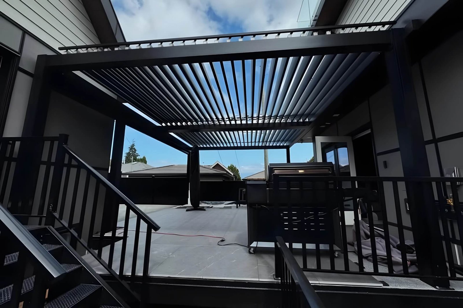 Bespoke bioclimatic motorized pergola with open louvers and integrated LED lighting, precisely installed between two existing residential buildings in NSW, Australia.