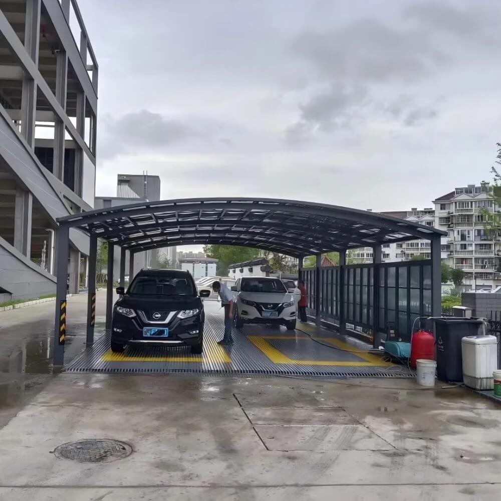 Heavy-duty dark grey aluminum carport featuring a large-span arched polycarbonate roof, providing weather protection for multiple vehicles in a commercial facility.