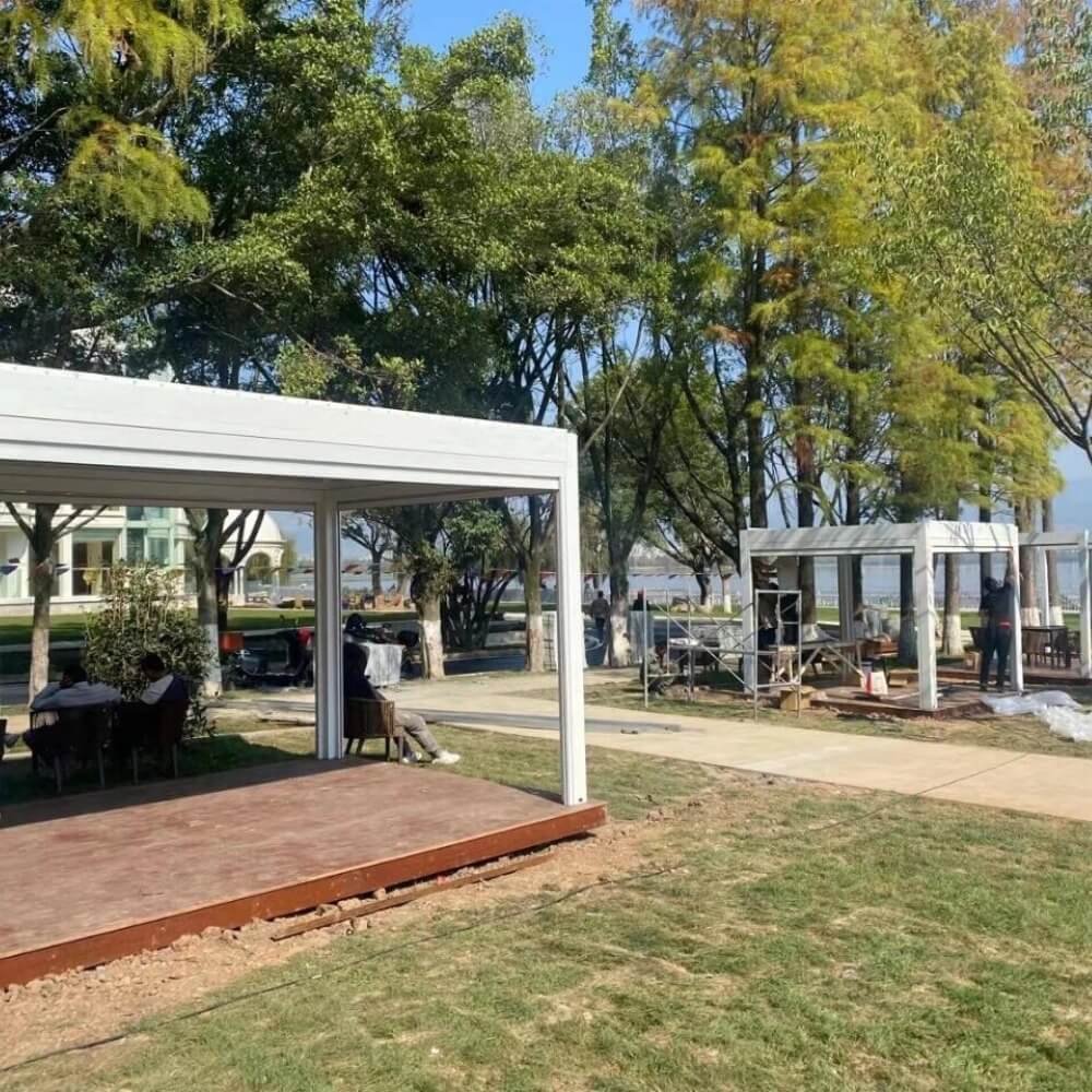Multiple white freestanding aluminum bioclimatic pergolas installed on wooden platforms in a public park in the USA, demonstrating commercial-grade outdoor shading solutions.