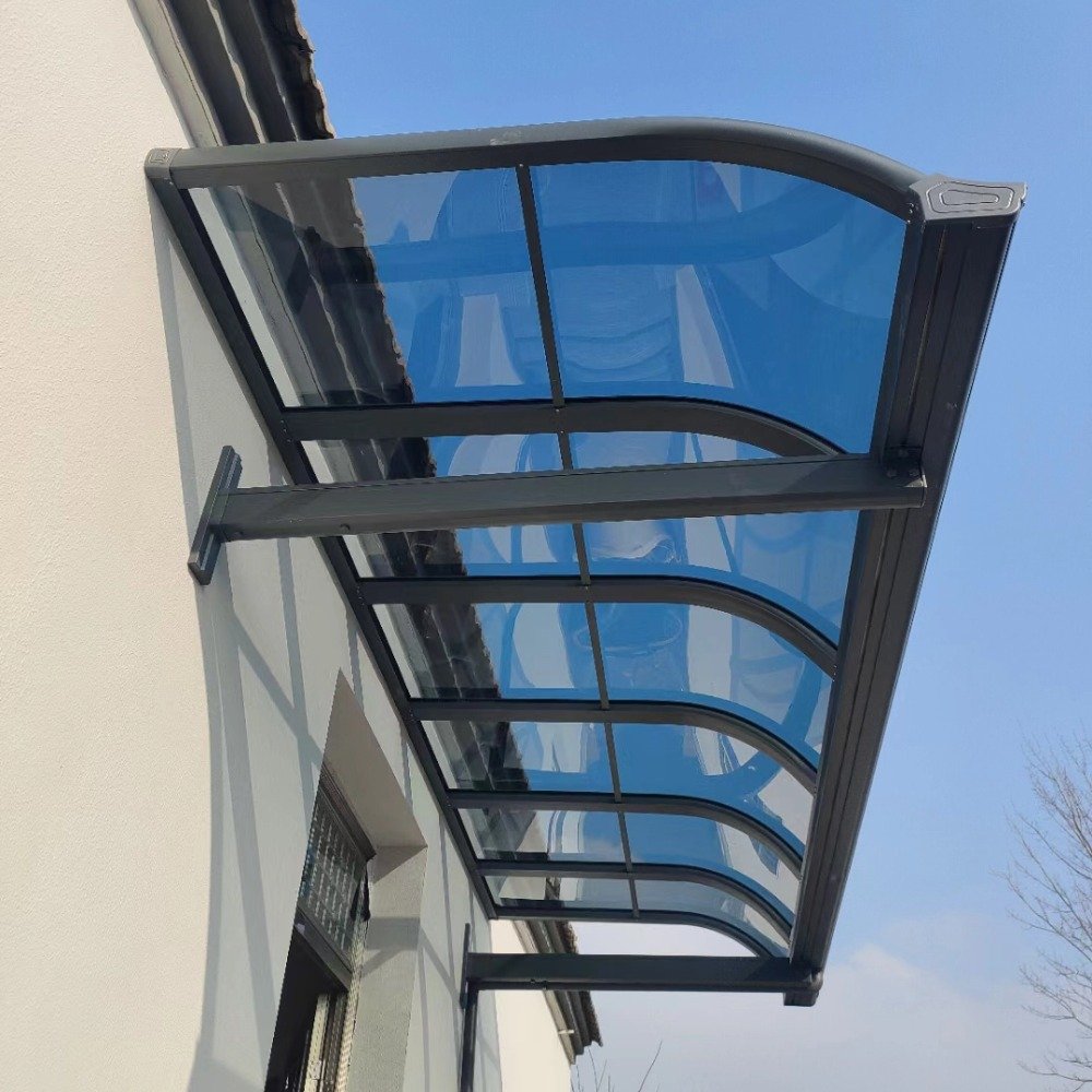Installed curved wall-mounted aluminum patio cover featuring a dark rust-proof frame and high-impact blue polycarbonate roof panels, demonstrating seamless facade integration.