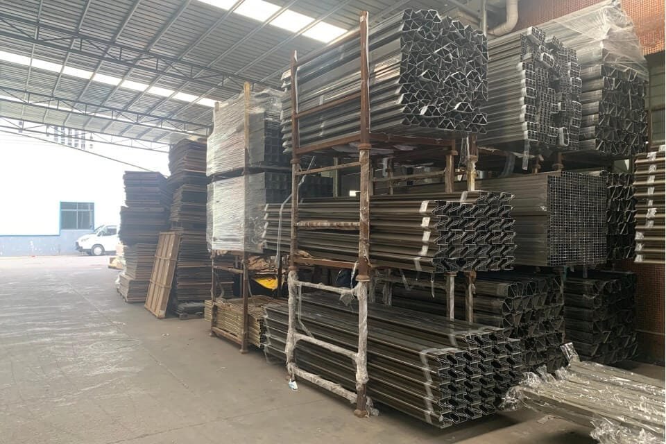 Organized multi-level inventory racks storing diverse custom aluminum extrusions and profiles, ready for the automated production of bioclimatic pergolas and carports.