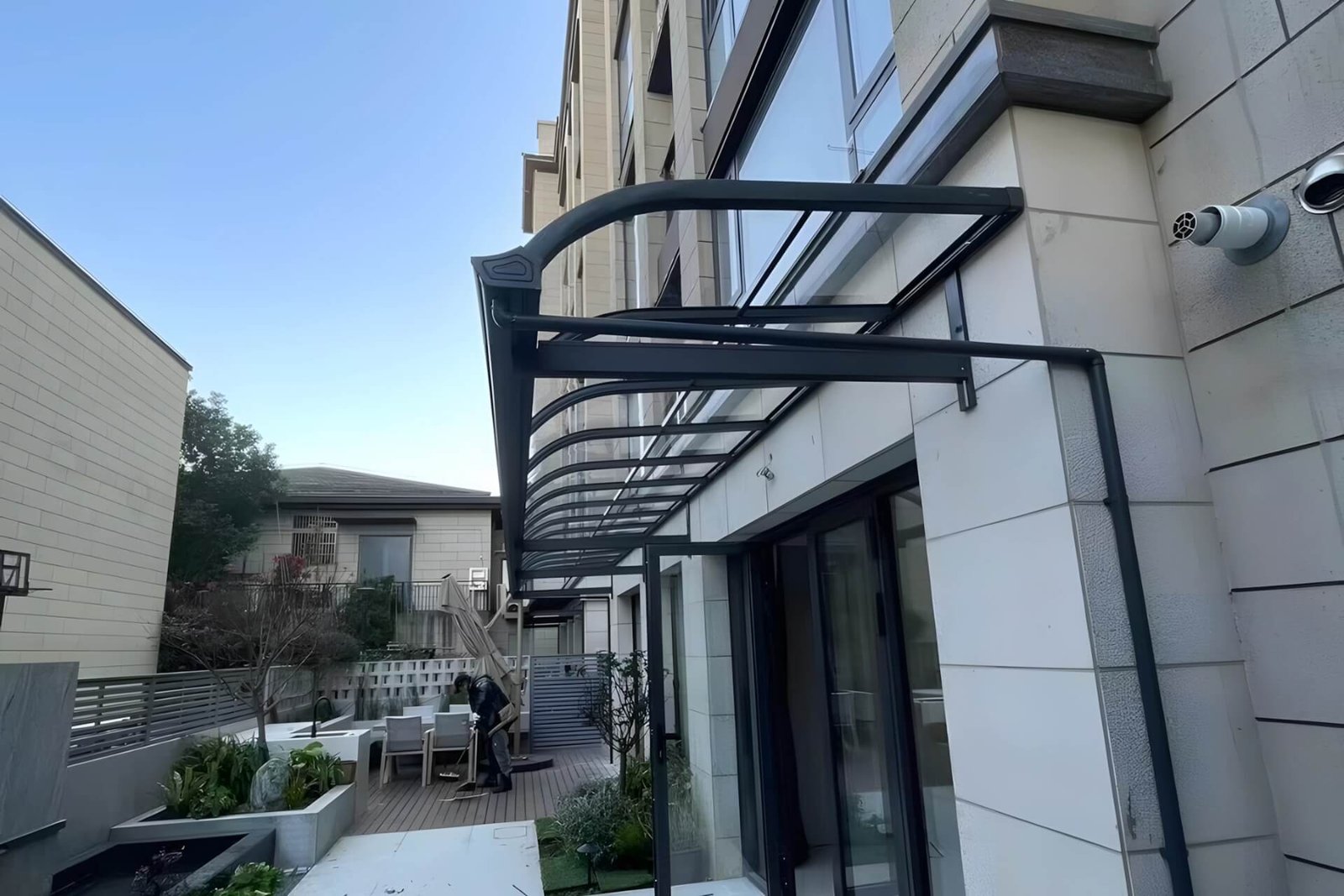 Custom dark grey aluminum patio awning with a curved design and high-transparency polycarbonate roof, seamlessly installed at a villa entrance in Foshan.