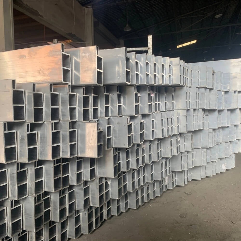 Massive stack of heavy-duty, multi-chambered raw aluminum extrusions used for structural pergola beams, demonstrating industrial-grade material strength and thickness.