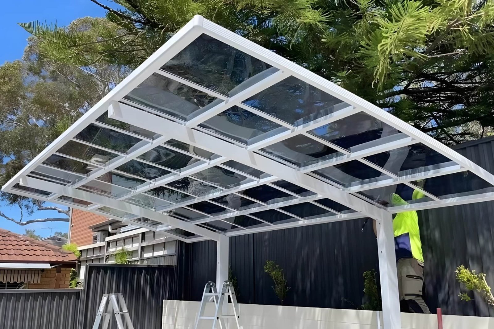 On-site installation of a heavy-duty white aluminum cantilever carport featuring tinted polycarbonate roof panels, demonstrating robust structural assembly and premium weather protection.