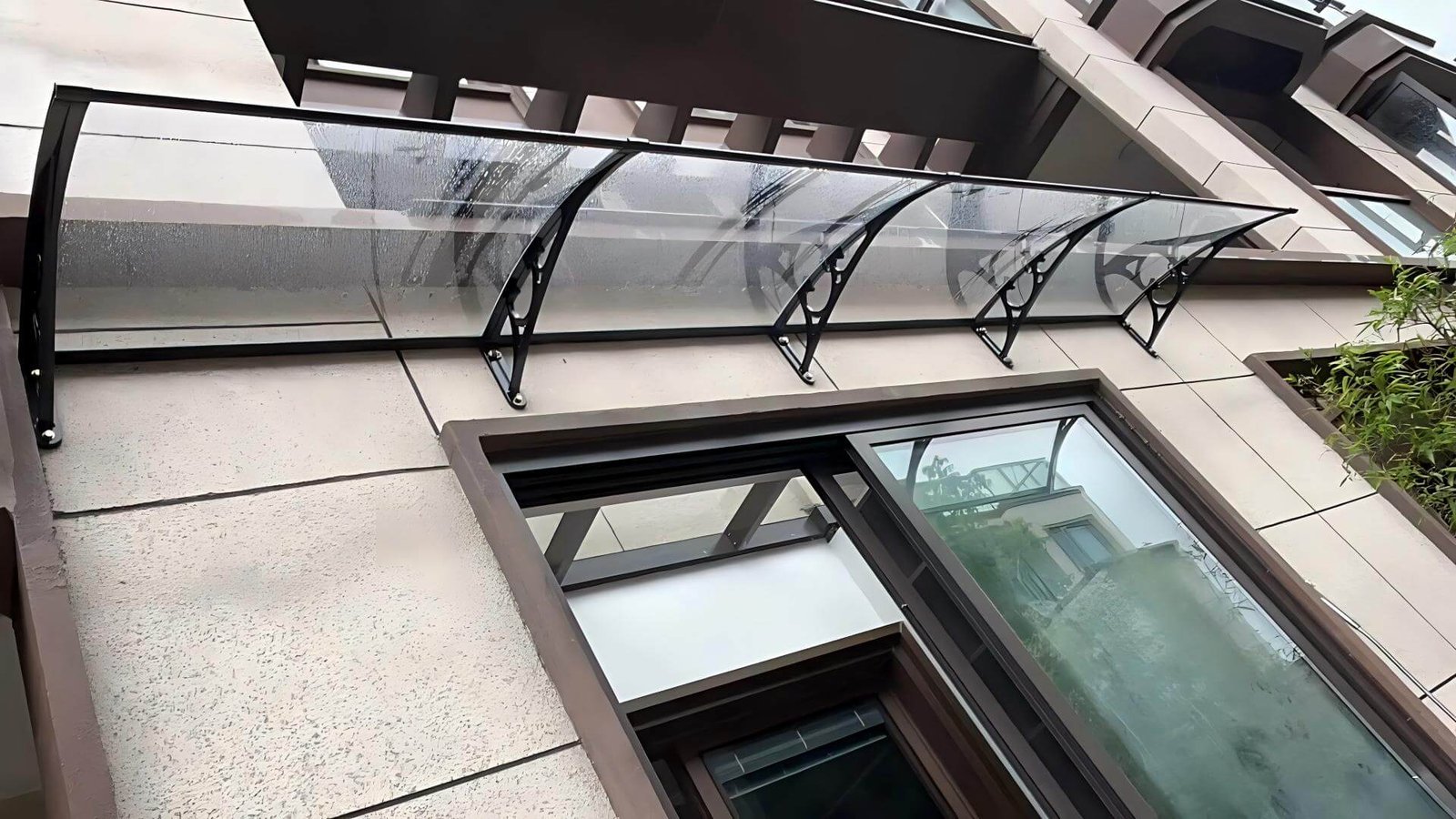 Real-world installation of a long clear polycarbonate window awning with black aluminum brackets on a modern building facade, demonstrating superior rain protection for architectural projects.