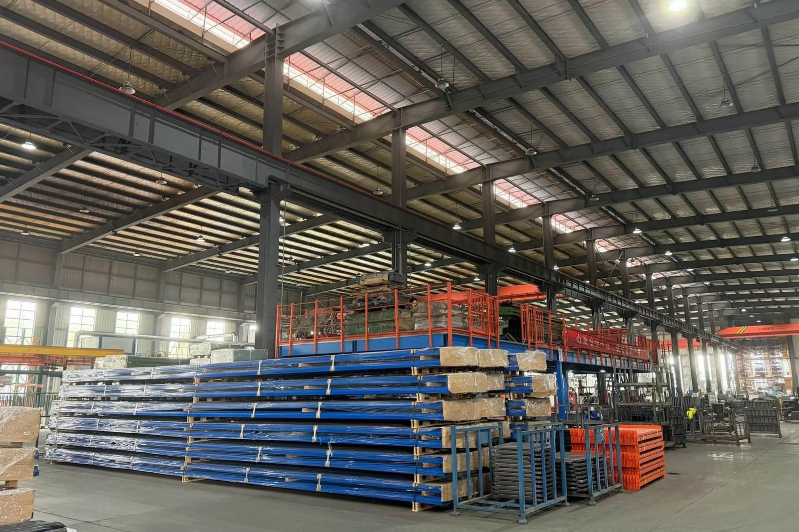 Expansive interior view of a modern aluminum manufacturing facility, showing neatly stacked aluminum extrusions and overhead cranes, representing high-volume production capacity for outdoor structures.
