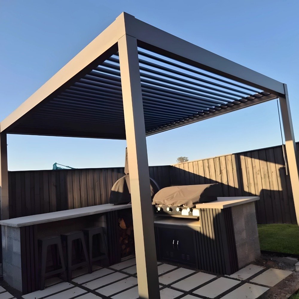 Freestanding manual bioclimatic aluminum pergola providing adjustable shade and weather protection for a backyard outdoor BBQ and kitchen station.