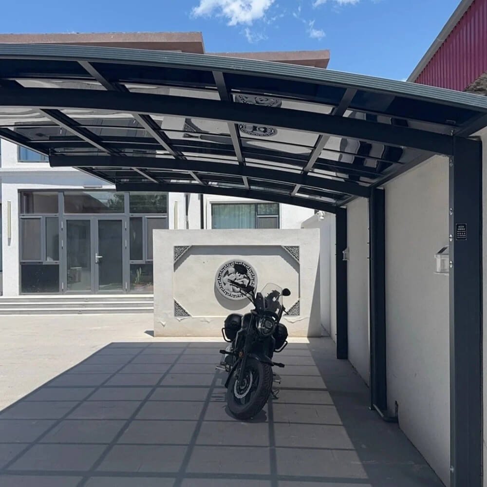 Modern dark grey cantilever aluminum carport featuring a space-saving single-column design and tinted polycarbonate roof, providing shelter for a motorcycle in a residential driveway.