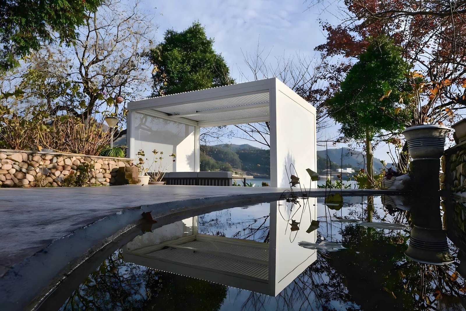 Stunning pure white freestanding aluminum bioclimatic pergola reflecting in a serene garden pool, showcasing the premium outdoor structures available directly from our manufacturing facility.