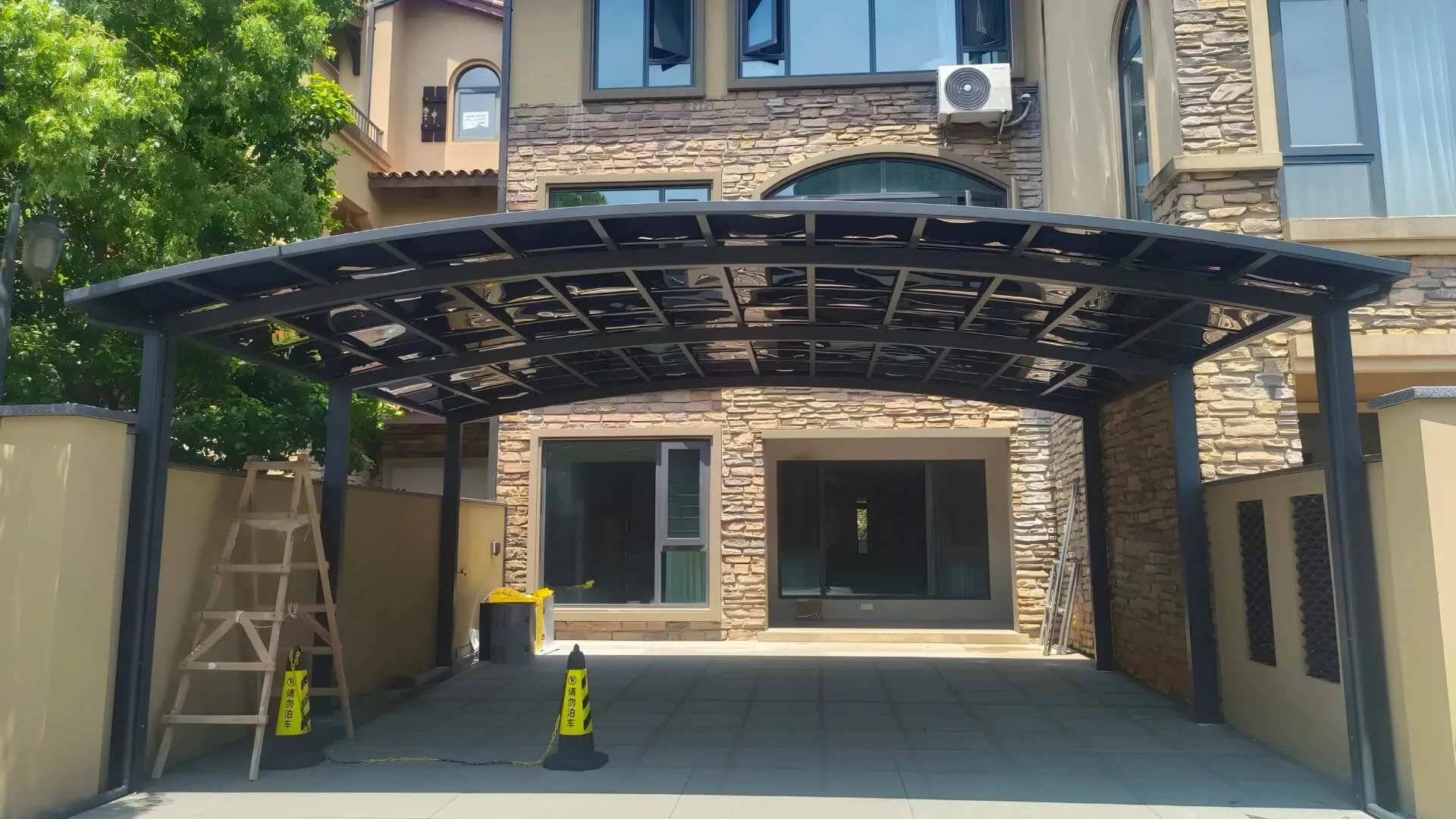 Real-world installation of a custom arched heavy-duty aluminum carport over a luxury residential driveway, featuring a dark frame and tinted UV-blocking polycarbonate roof panels.