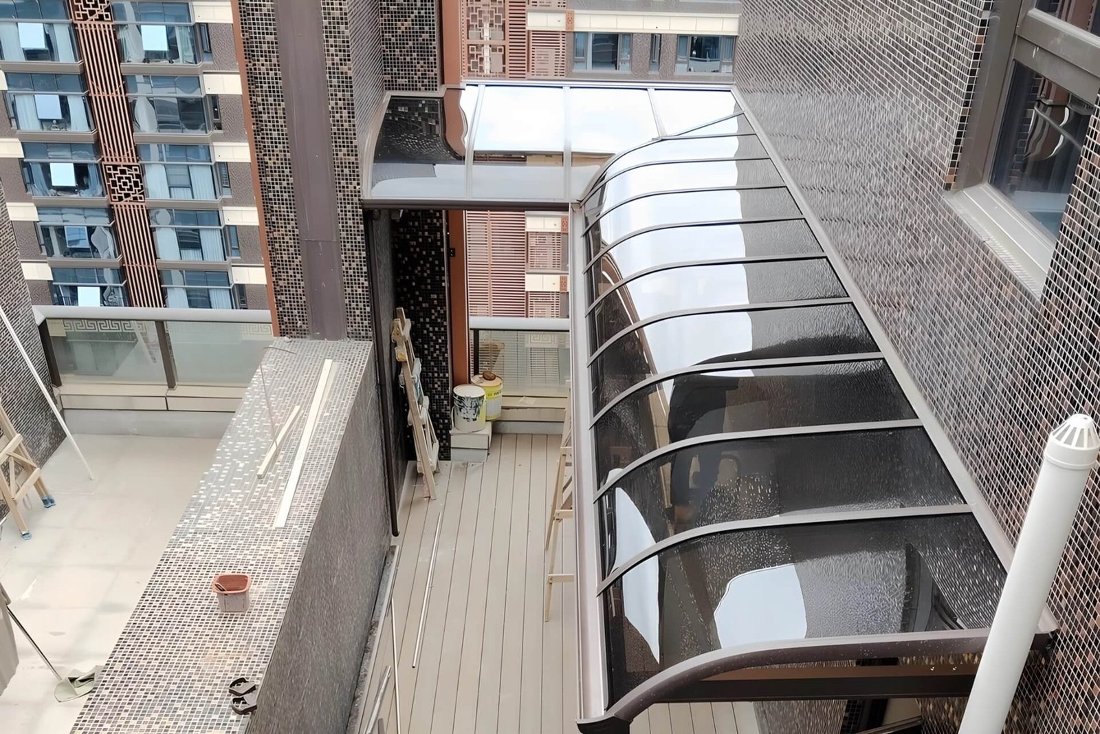 A top-down view of a custom L-shaped aluminum patio cover installed on a spacious high-rise balcony, featuring tinted impact-resistant polycarbonate panels and a seamless 90-degree corner.