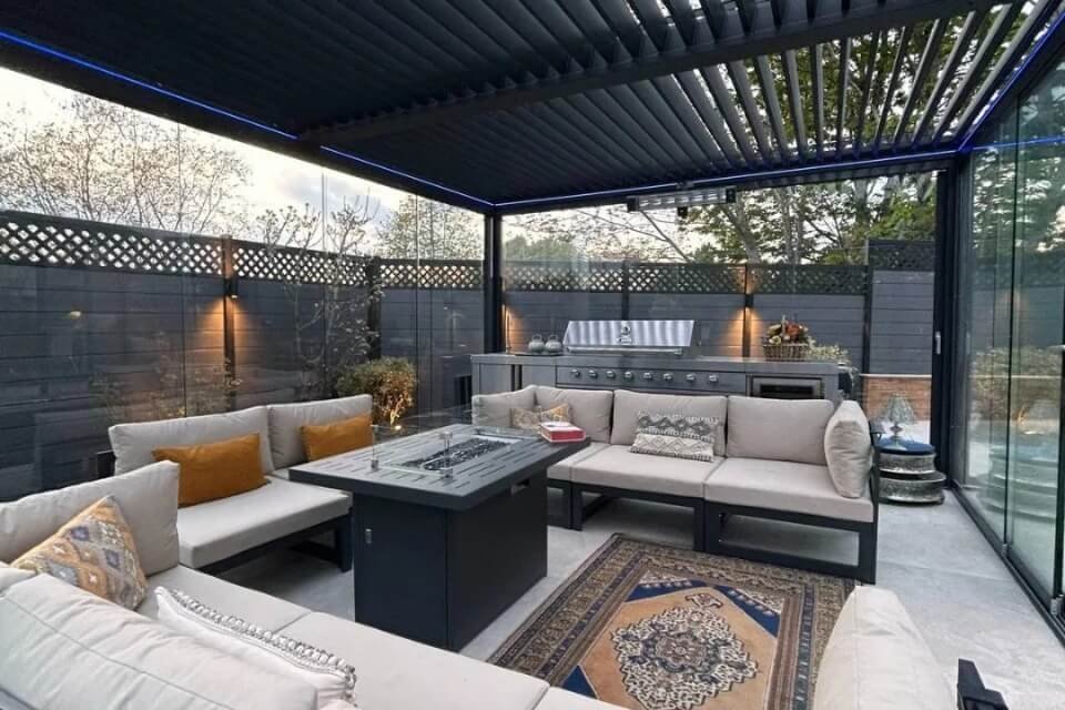 glass enclosed louvered pergola featuring an outdoor kitchen and dining setup for year round entertainment