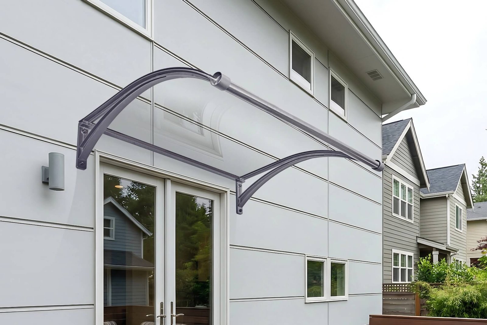 A modern arched aluminum door canopy with clear polycarbonate panels installed above residential double patio doors, providing elegant all-weather protection for the entrance.