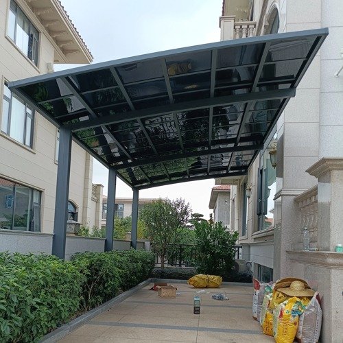 A modern cantilever aluminum carport installed next to a residential villa, featuring a space-saving single-sided post design and UV-blocking polycarbonate roof.